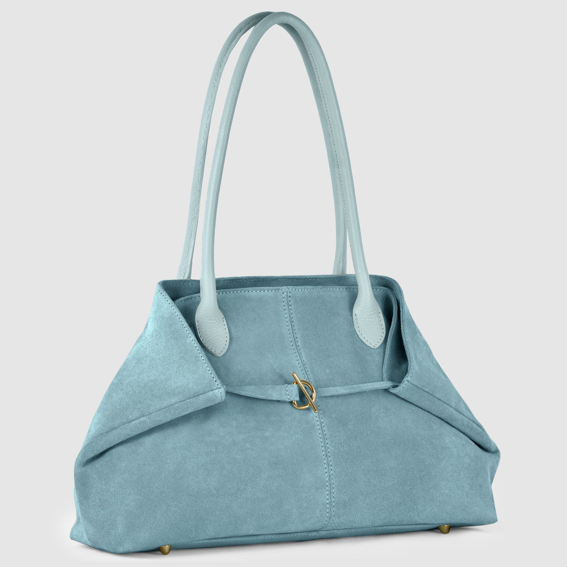 A light blue Italian-crafted suede tote bag with long handles, a front pocket, and a gold clasp detail, shown against a plain light background. The structured design combines elegance with a soft texture for timeless appeal.