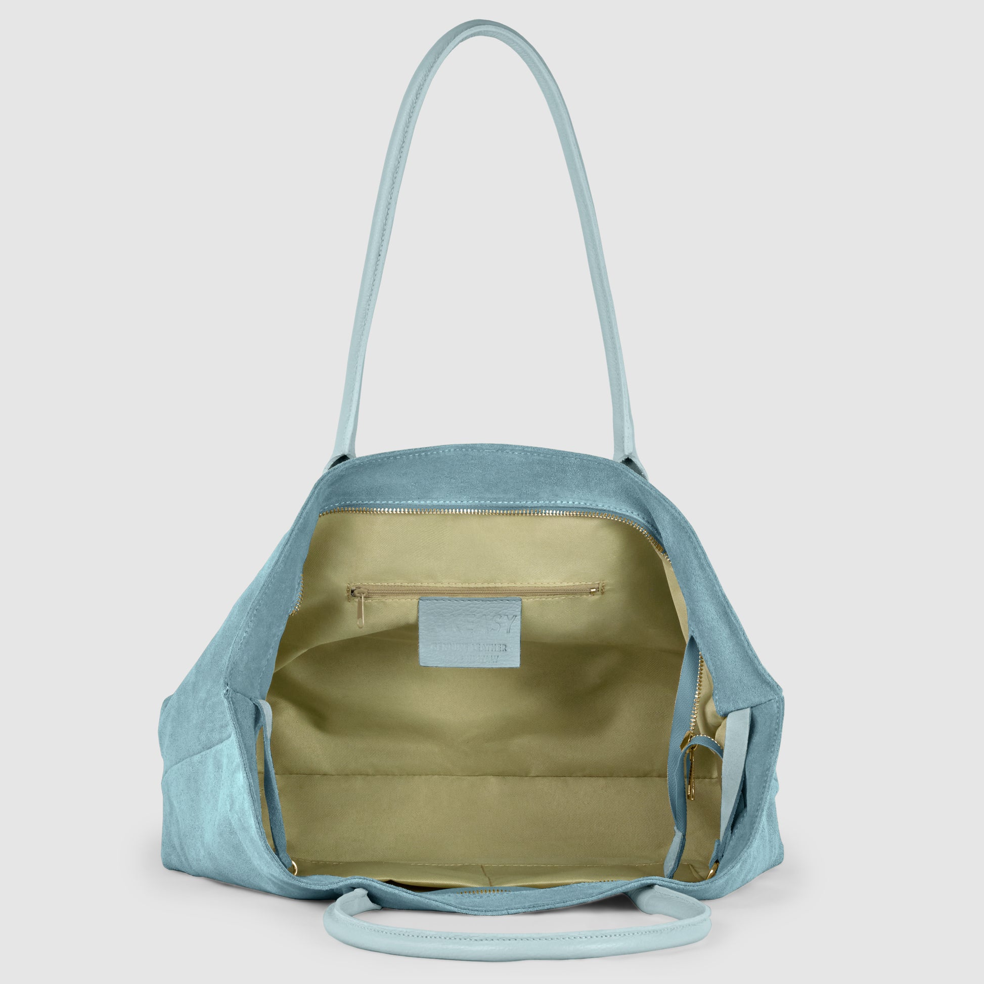 A light blue genuine leather shoulder bag with long handles is shown open, revealing a spacious beige interior with a zippered pocket and a small label inside. The bag is empty and sits upright against a plain background.