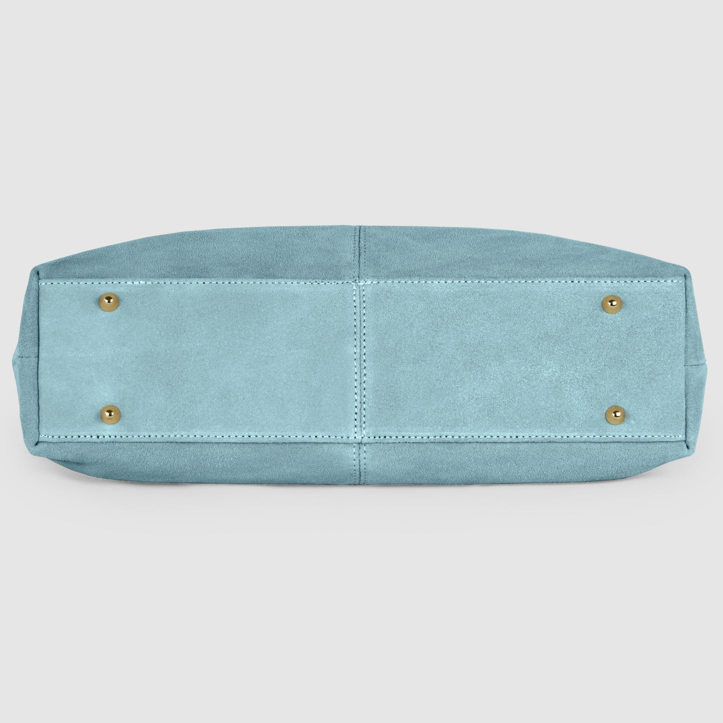 A light blue suede tote bag viewed from the bottom, featuring two stitched panels and four gold metal feet, on a plain white background.