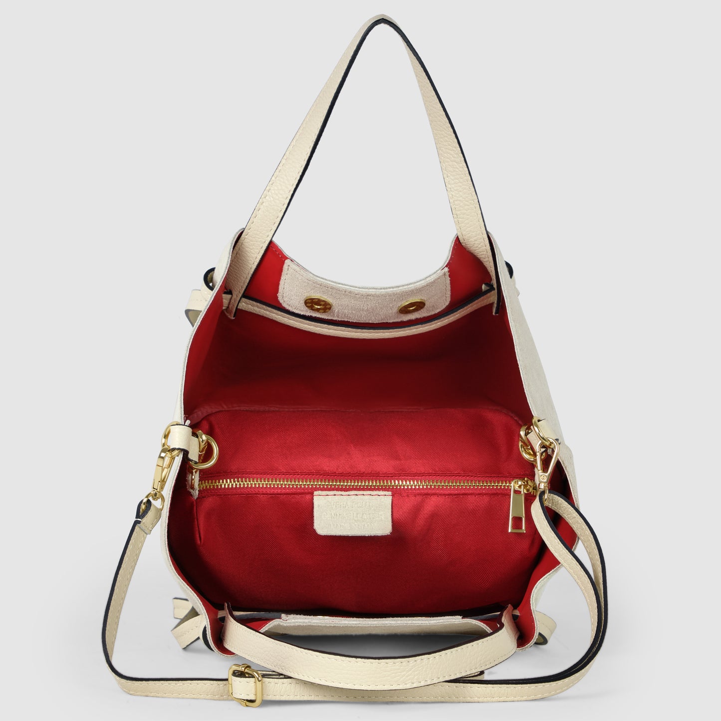 A cream-colored handmade tote with gold hardware and a detachable strap, opened to reveal a spacious interior lined in bright red fabric with a zippered pocket and snap closures.