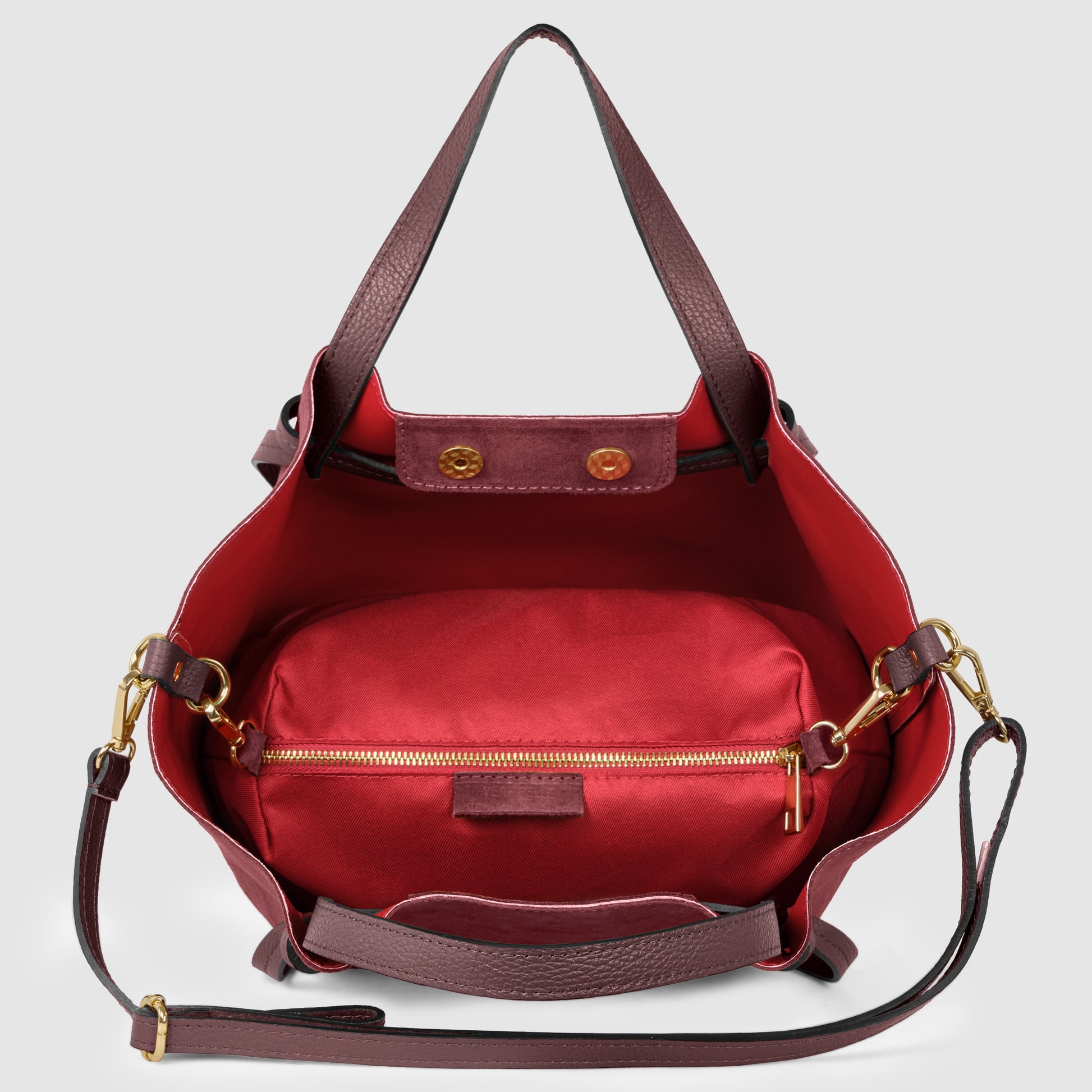 Open burgundy handmade Italian bag with a red interior, featuring a large zippered pouch inside, gold hardware, long adjustable strap, and two short handles, displayed against a light gray background.