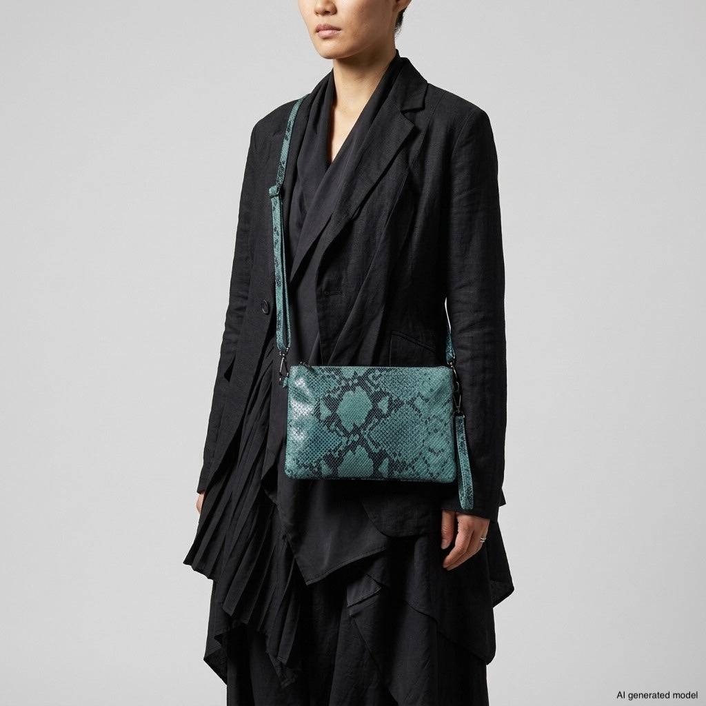 A person wearing a layered black outfit stands against a plain background, carrying a striking python-embossed crossbody purse made in Italy.