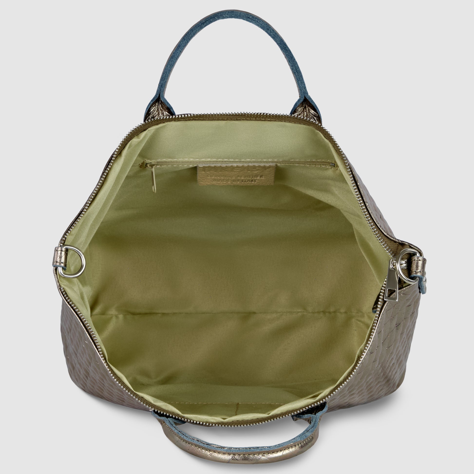 A handcrafted Italian handbag with a textured outer surface is shown open, revealing a spacious interior lined with light green fabric, a zippered inner pocket, and silver hardware on the sides and handles.