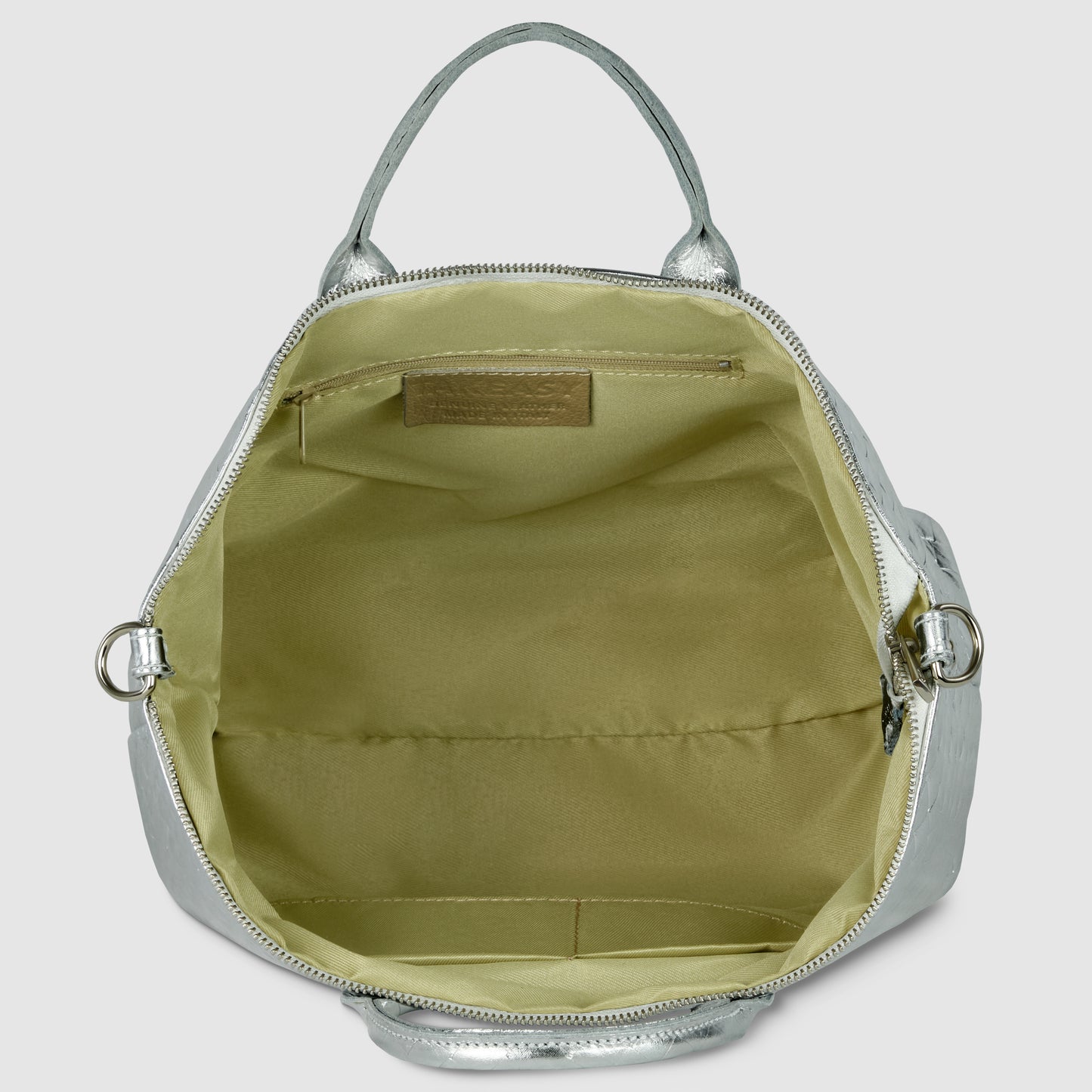 A metallic silver handcrafted Italian handbag with its top zipper open, revealing a beige fabric-lined interior with a flat inner pocket and an embossed leather label above the pocket. The bag has silver hardware and two handles.
