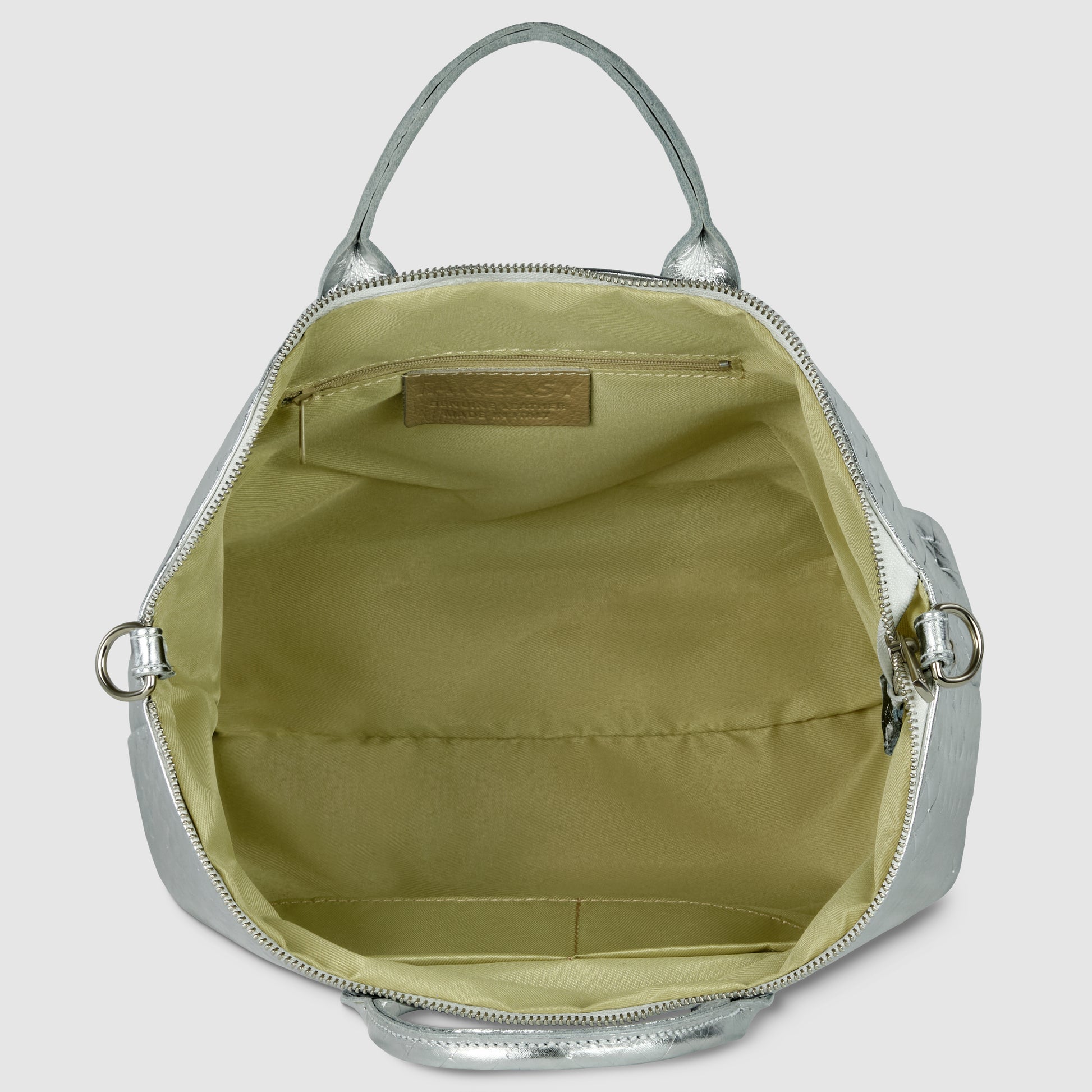 A metallic silver handcrafted Italian handbag with its top zipper open, revealing a beige fabric-lined interior with a flat inner pocket and an embossed leather label above the pocket. The bag has silver hardware and two handles.