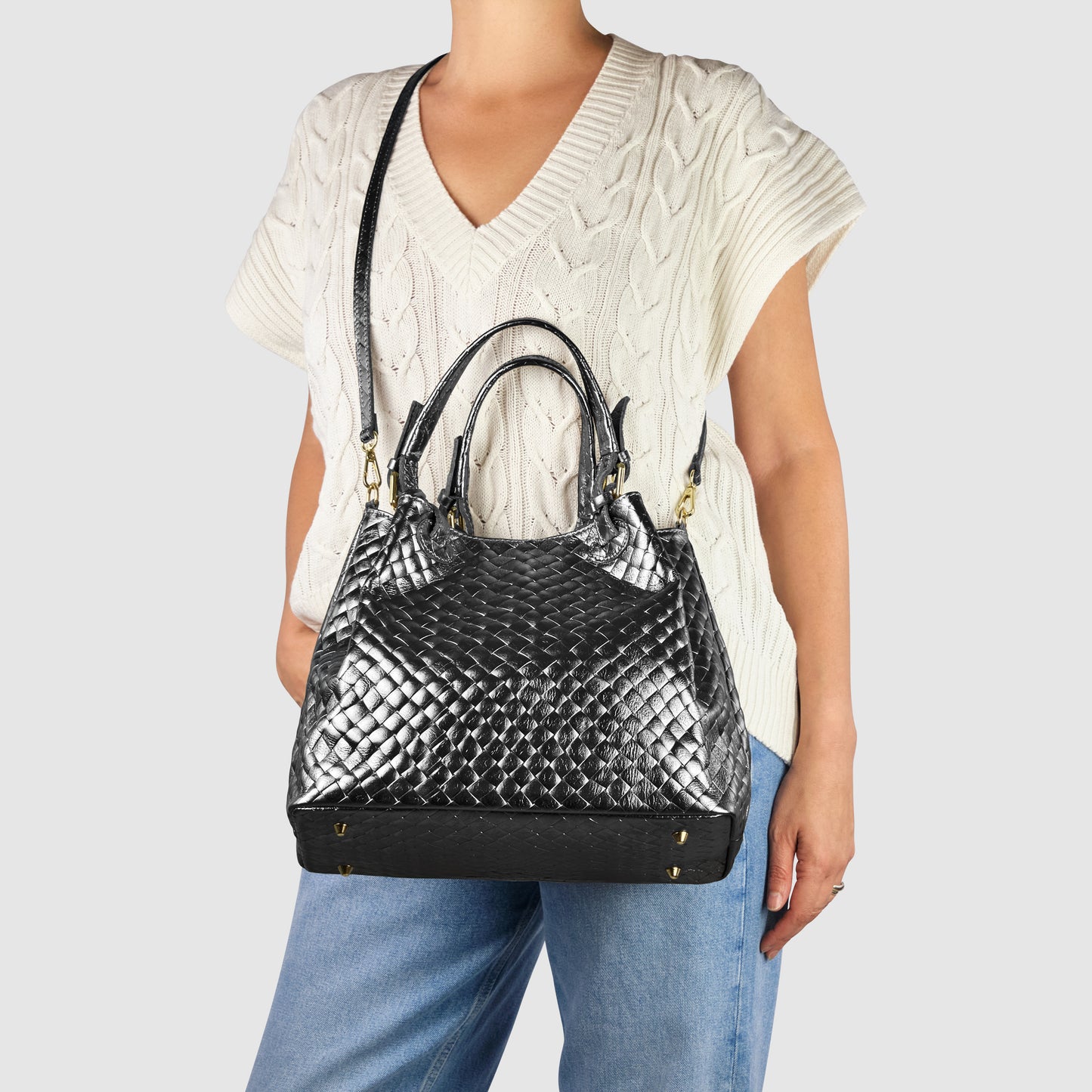 A person wearing a cream cable-knit short-sleeve sweater and blue jeans carries a large Italian-made handbag crafted from black woven leather, featuring dual handles and a shoulder strap.
